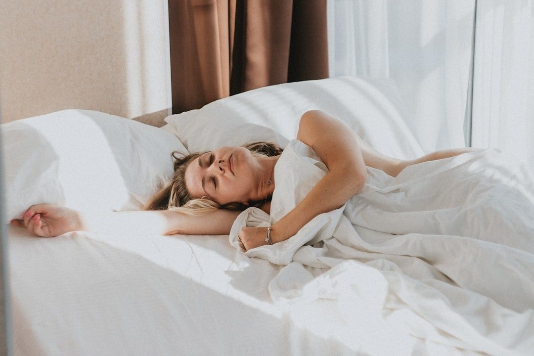 Kvinna ligger vaken i en ljus säng med slutna ögon