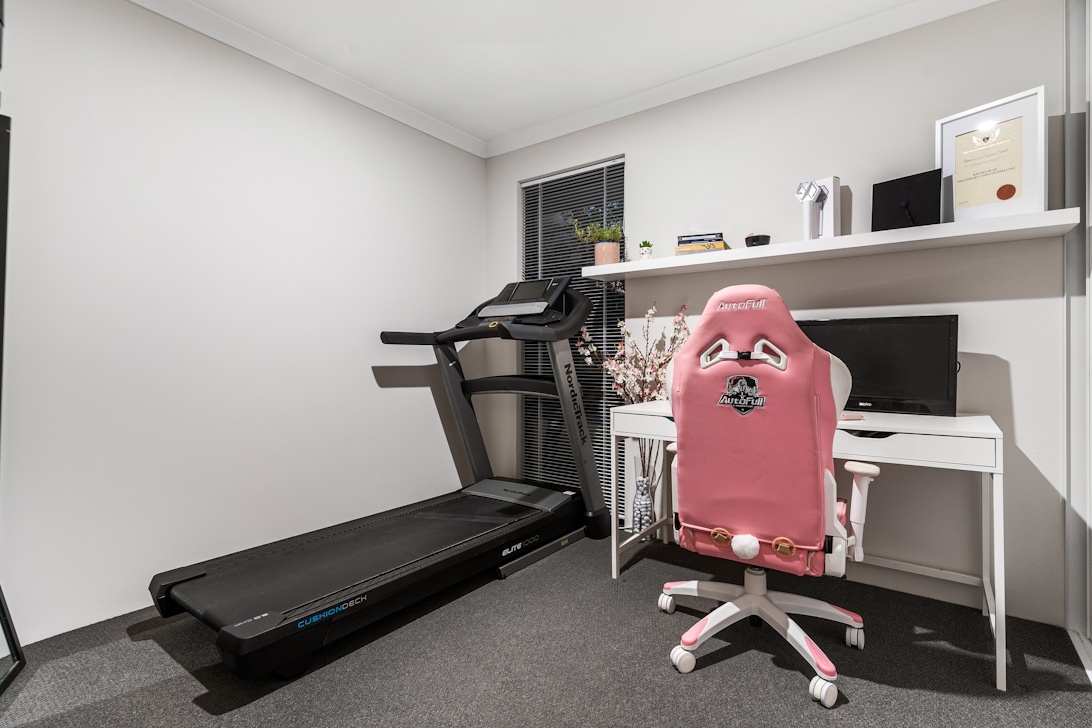 Ett litet hemmakontor som också fungerar som gym, med ett löpband bredvid skrivbordet.