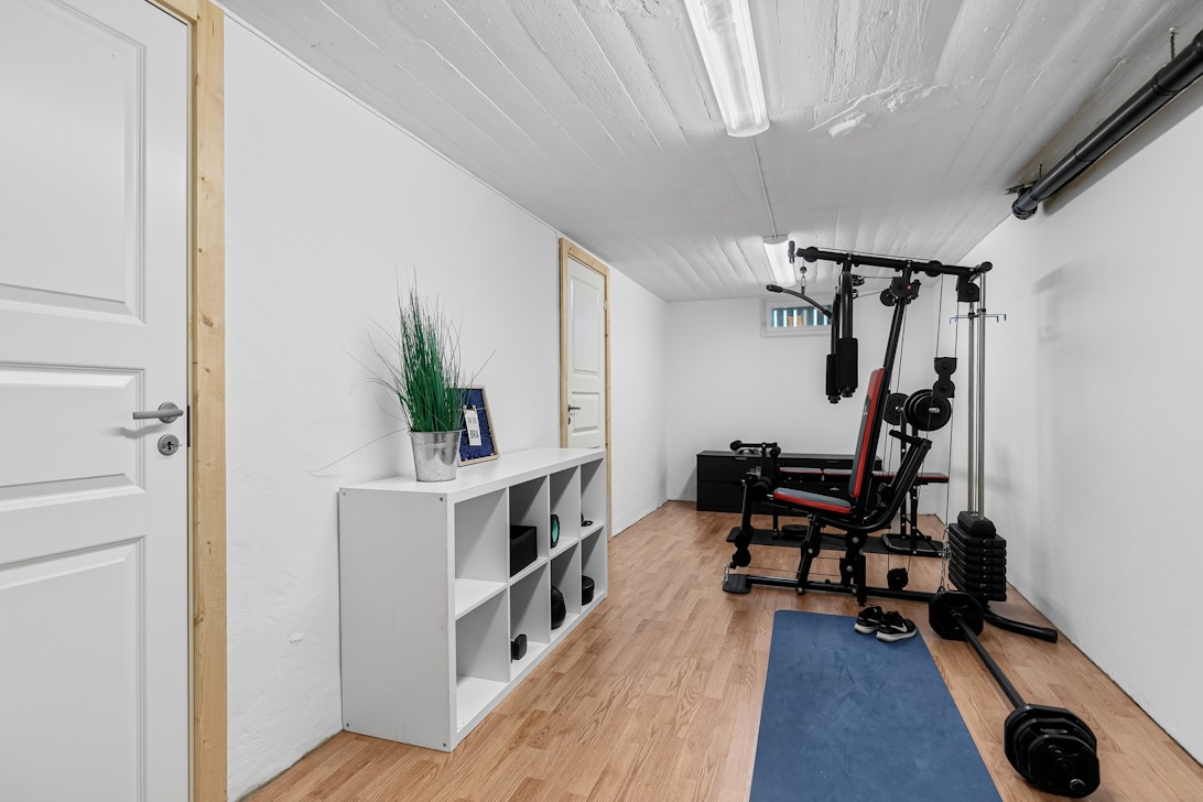 Ett välorganiserat hemmagym i en källare med en multistation, fria vikter och förvaringshyllor.