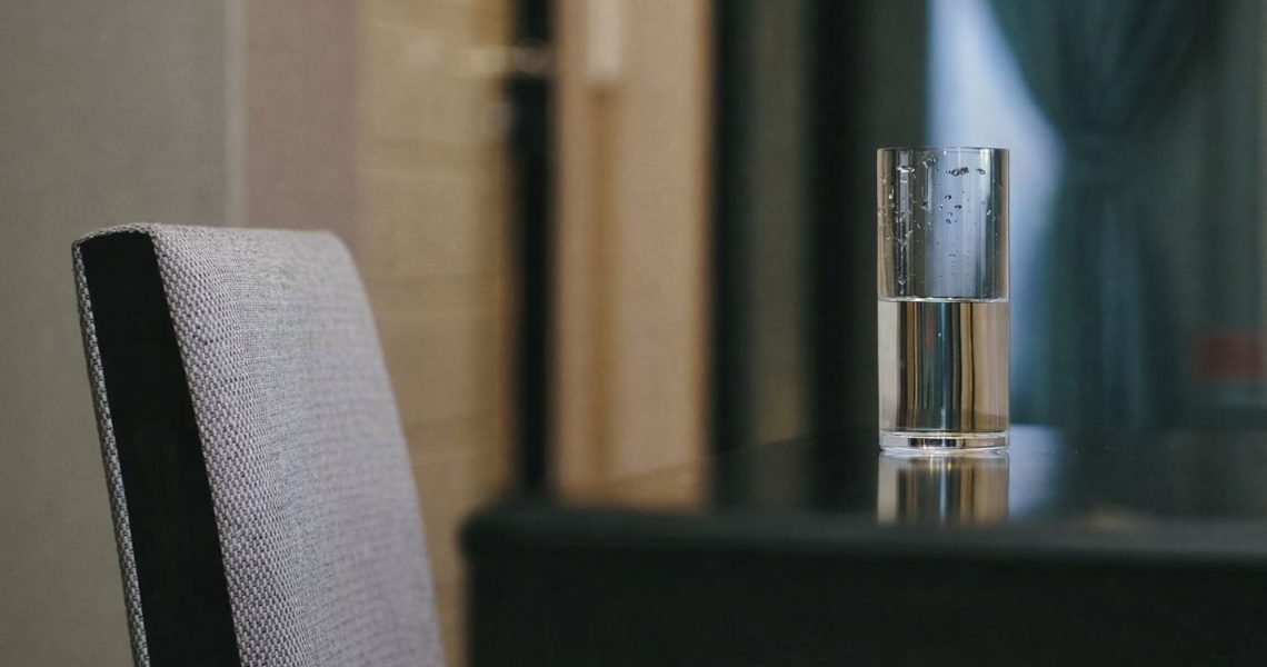 Vattenglas på bord, med en stol i förgrunden – symboliserar lugn och eftertanke.