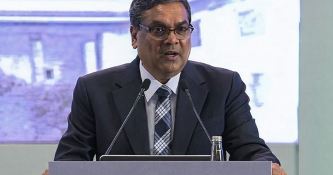 En man talar vid en talarstol, med mikrofoner framför sig och en suddig bakgrund.